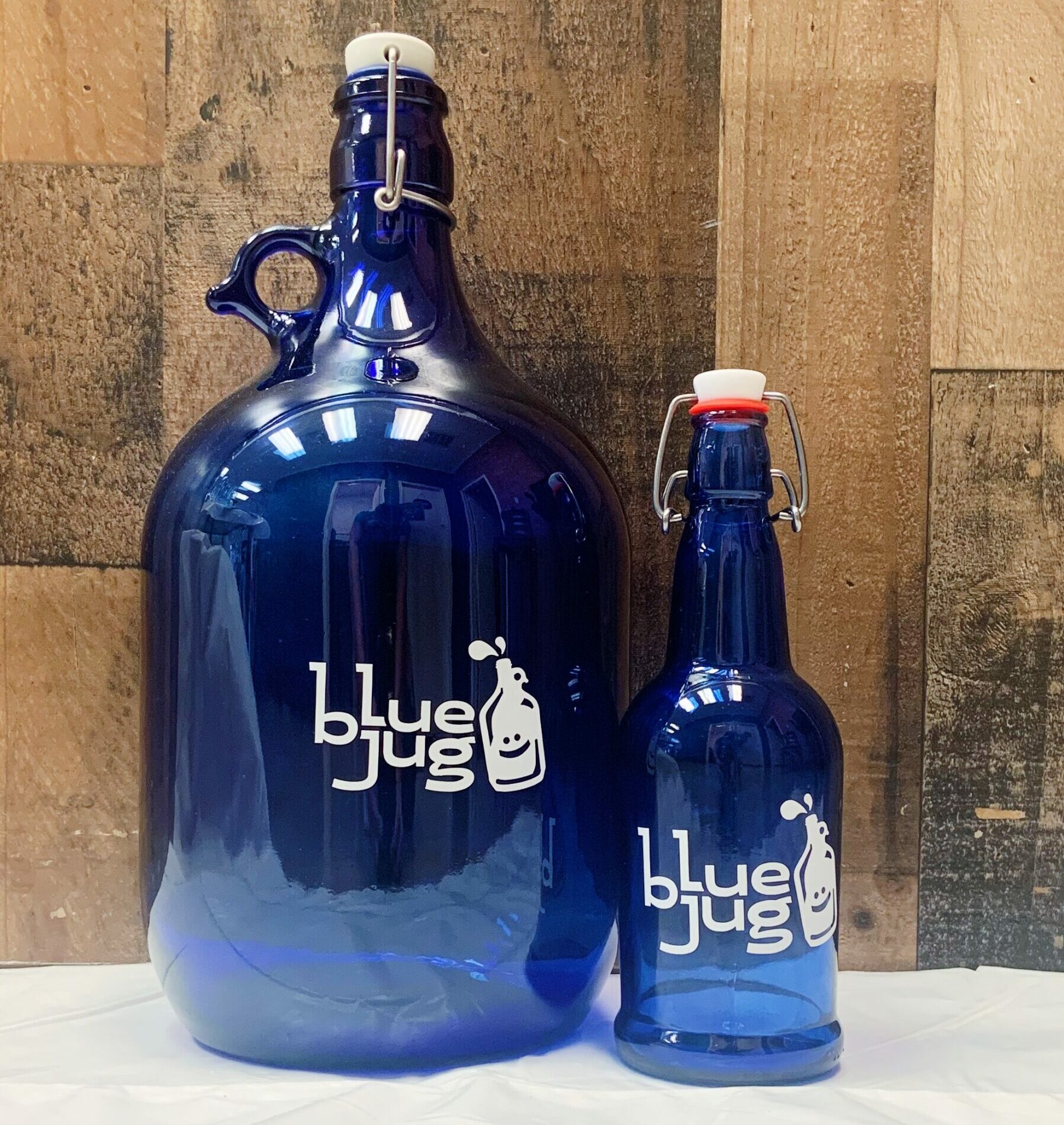 Two ‘Blue Jug’ bottles in dark blue glass against a rustic wooden backdrop
