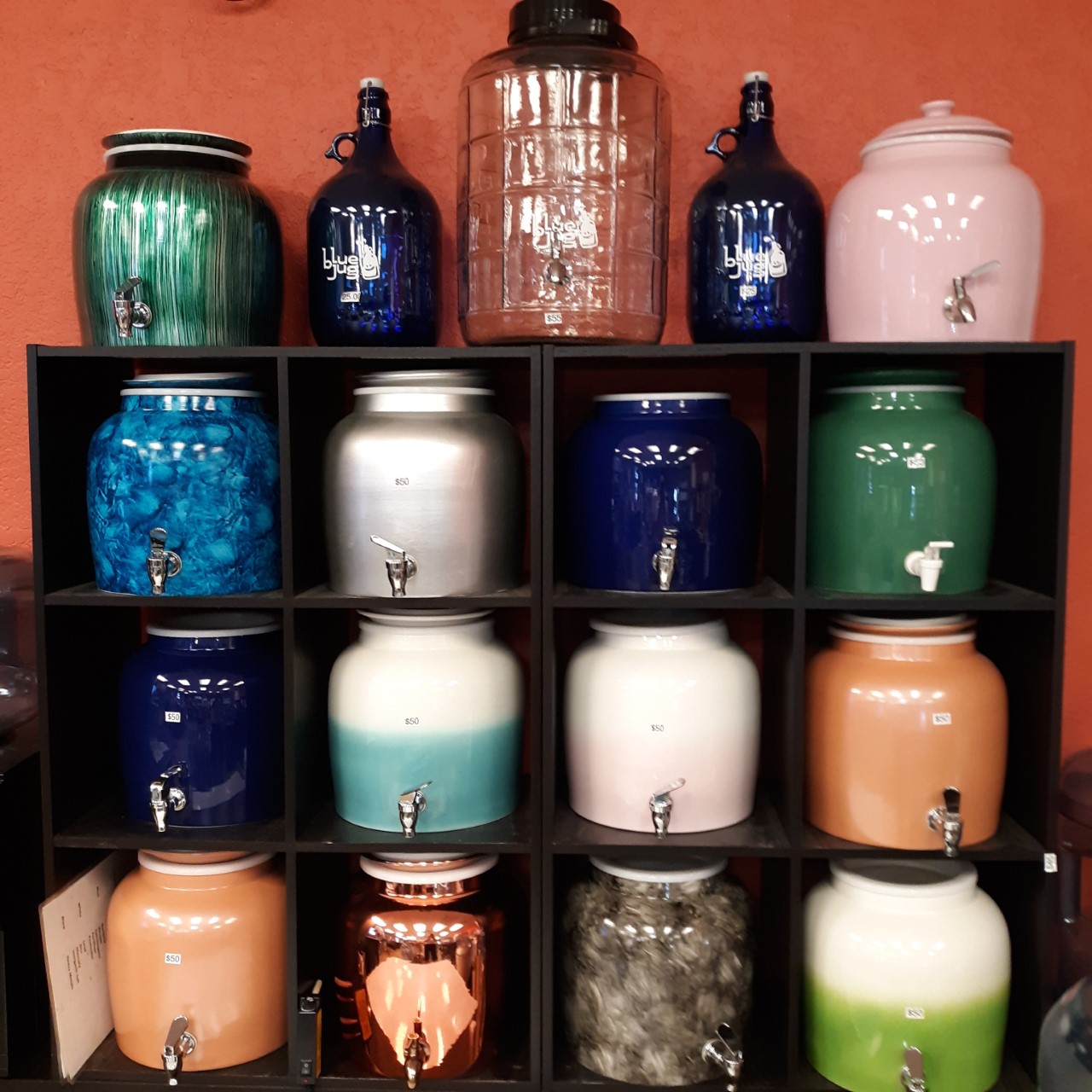 Set of vibrant water jars in various colors, elegantly displayed on a stand. Each jar features a unique hue, adding a pop of color to any space