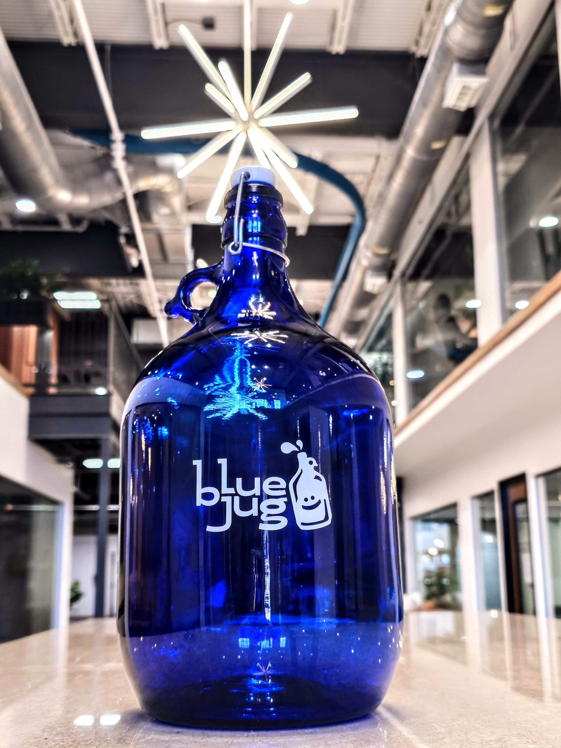 A dark blue bottle placed on tiles under the factory with heavy lights, featuring the "Blue Jug Waco" logo