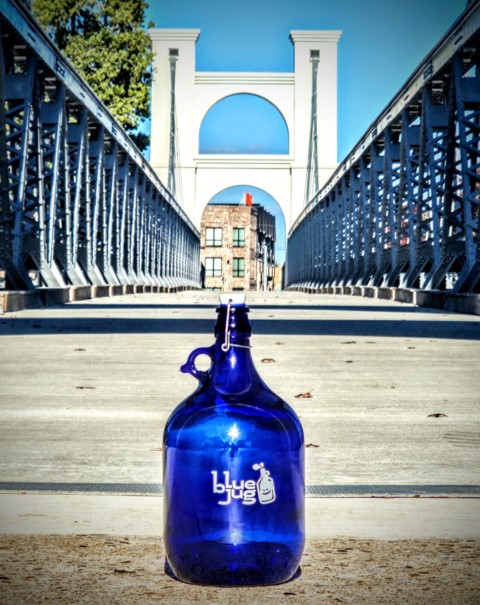 A dark blue can placed on a suspension bridge with "Blue Jug Waco" Logo on it